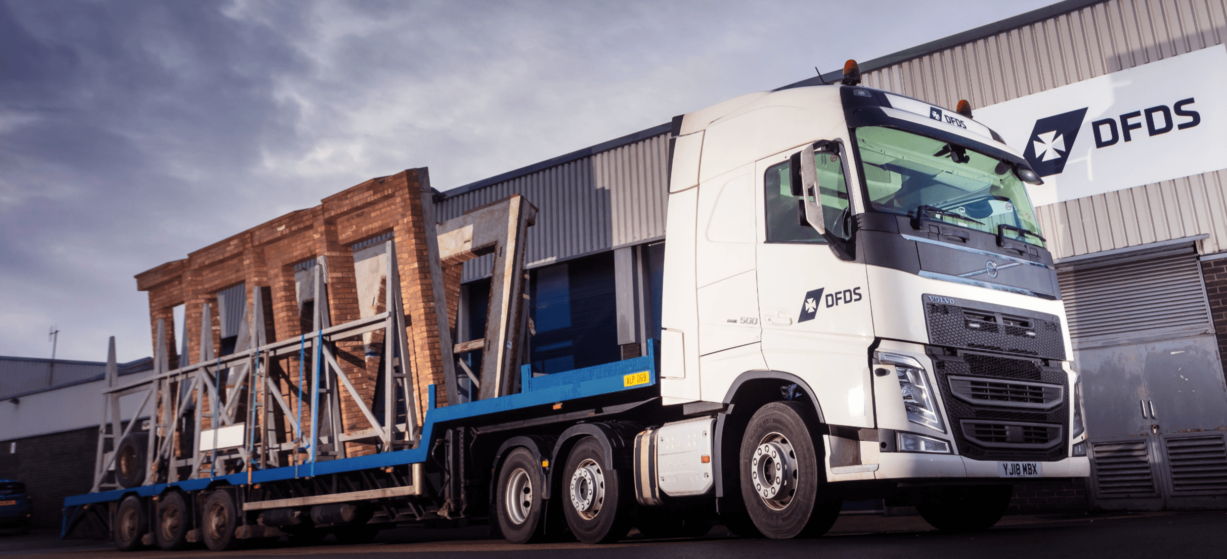 A DFDS truck transporting an assembled façade parked in front of a DFDS warehouse