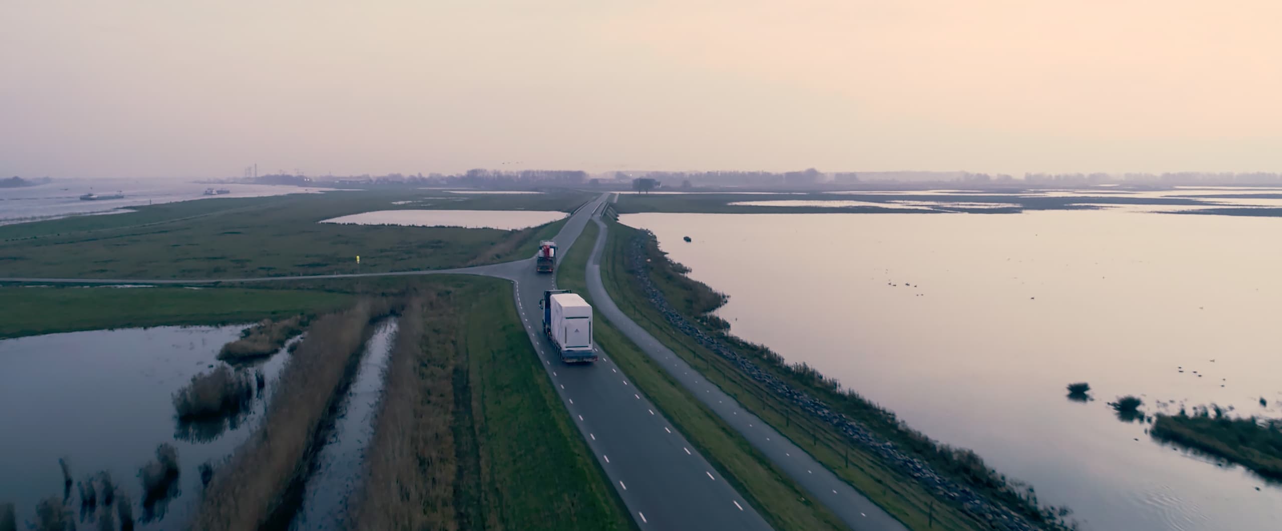 Aerial view of two trucks driving on a road among wetlands at dawn