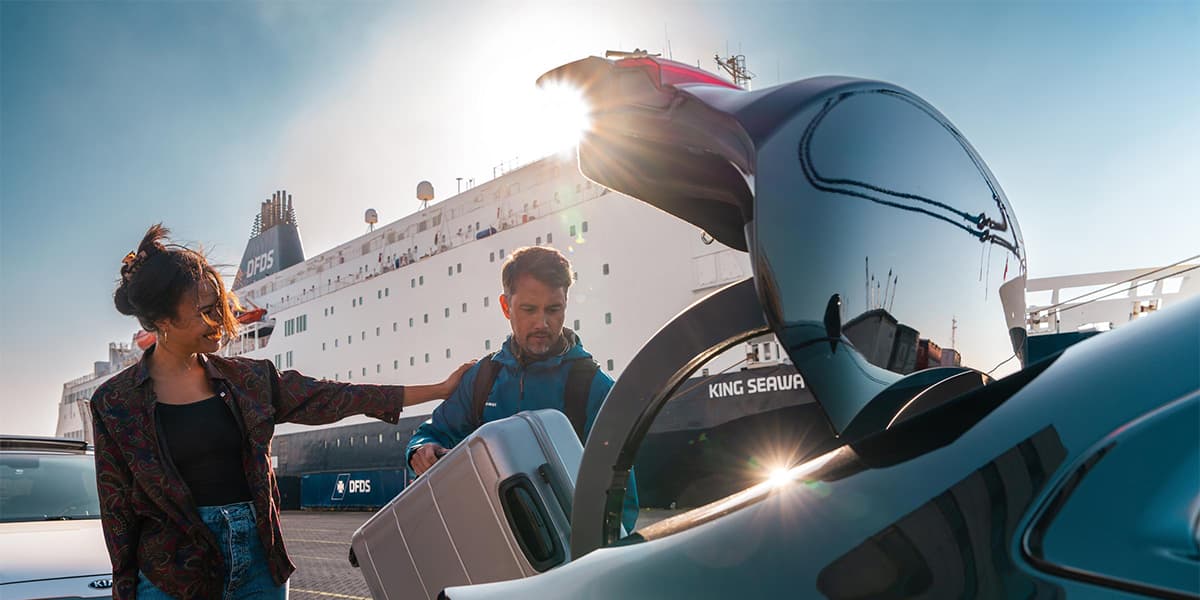 Couple packing car with bags with DFDS ship in the background