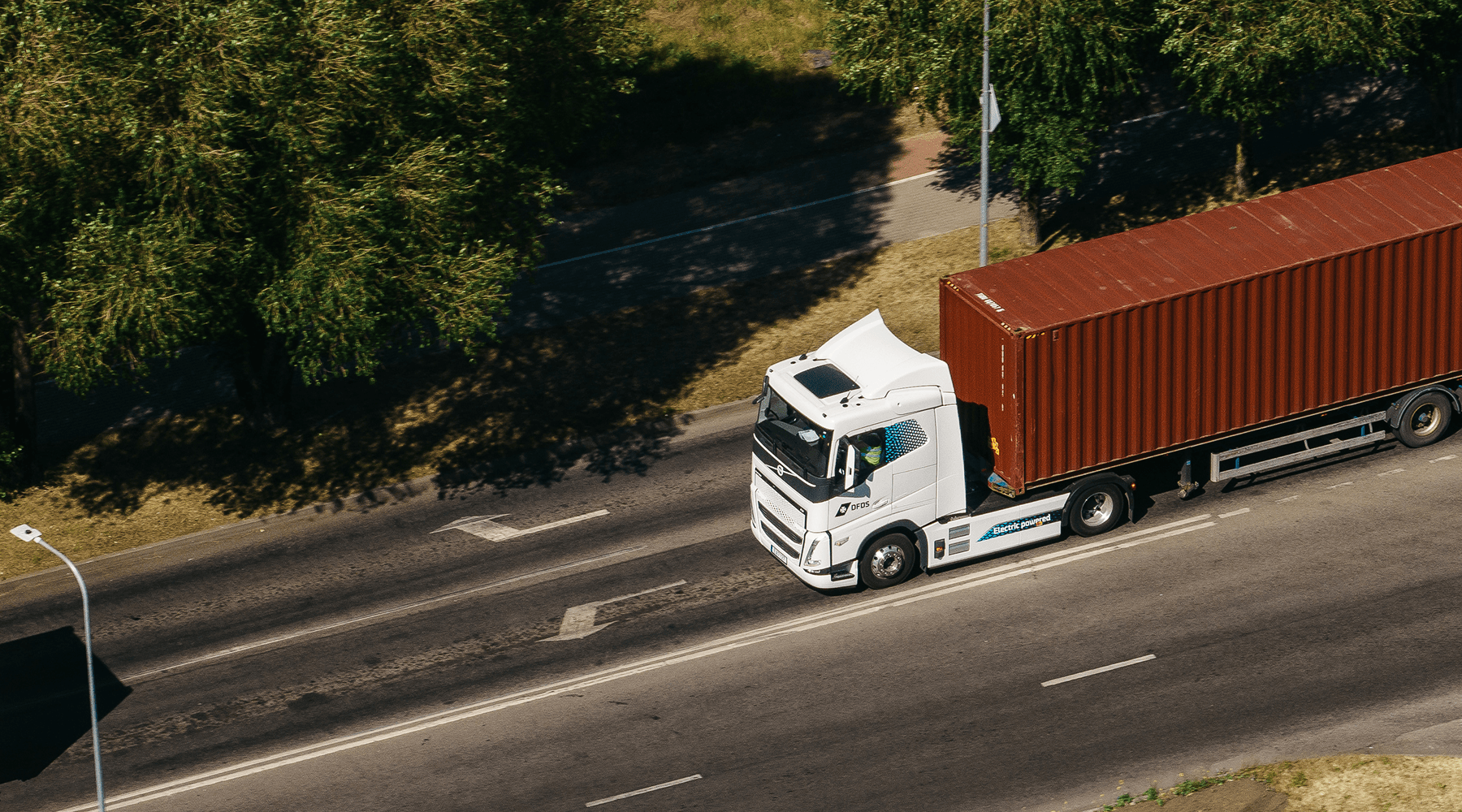 An electric DFDS truck, with a container on a trailer, driving on a highway in the Klaipėda region