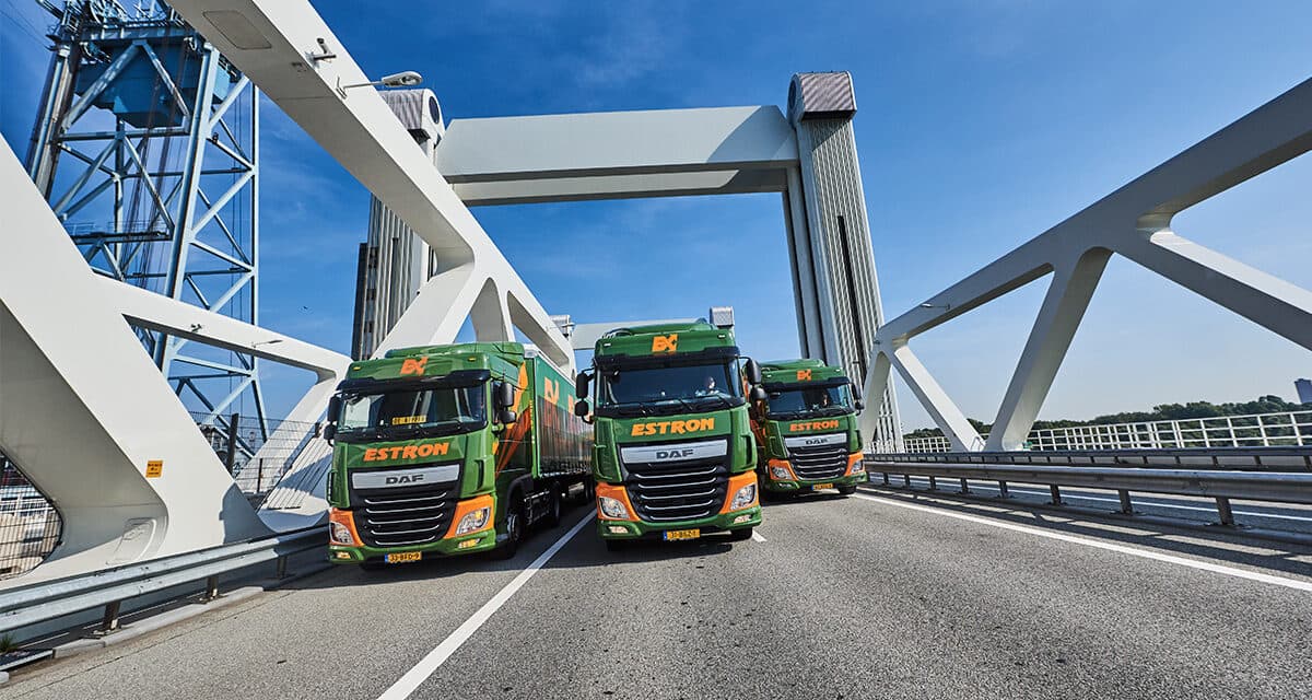 Three Estron trucks, in their green & orange livery, driving next to each other on a bridge