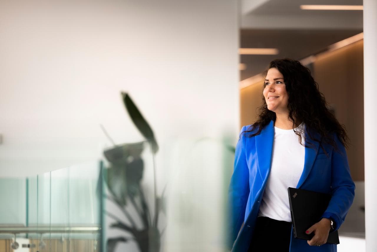Hallway in new DFDS headquarter, woman in white shirt and blue jacket, walking with laptop in left hand, smiling