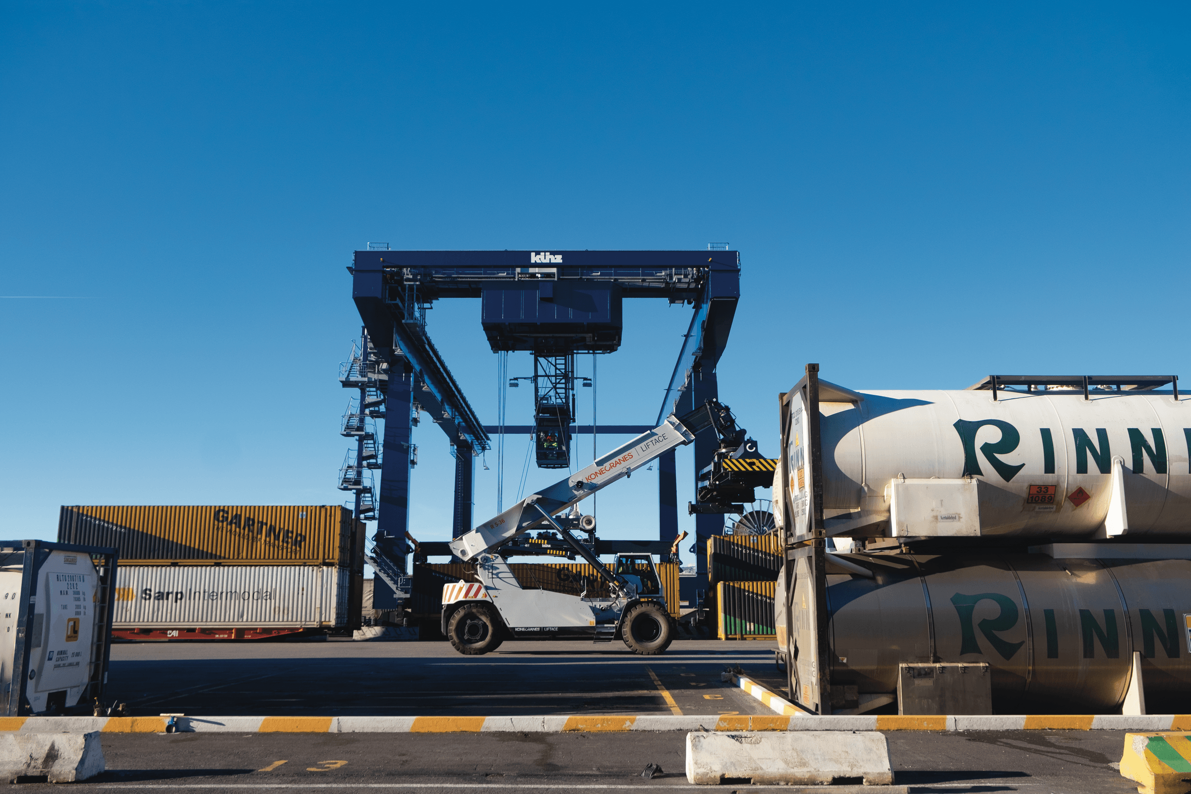 A reach stacker vehicle moving containers towards a crane at the DFDS Freight terminal in Trieste