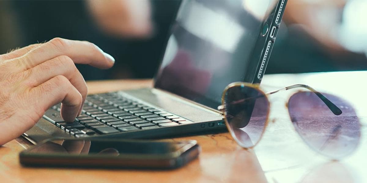 Photo of a person's hand on a black laptop with a mobile phone and sunglasses to represent Wifi onboard DFDS ferry