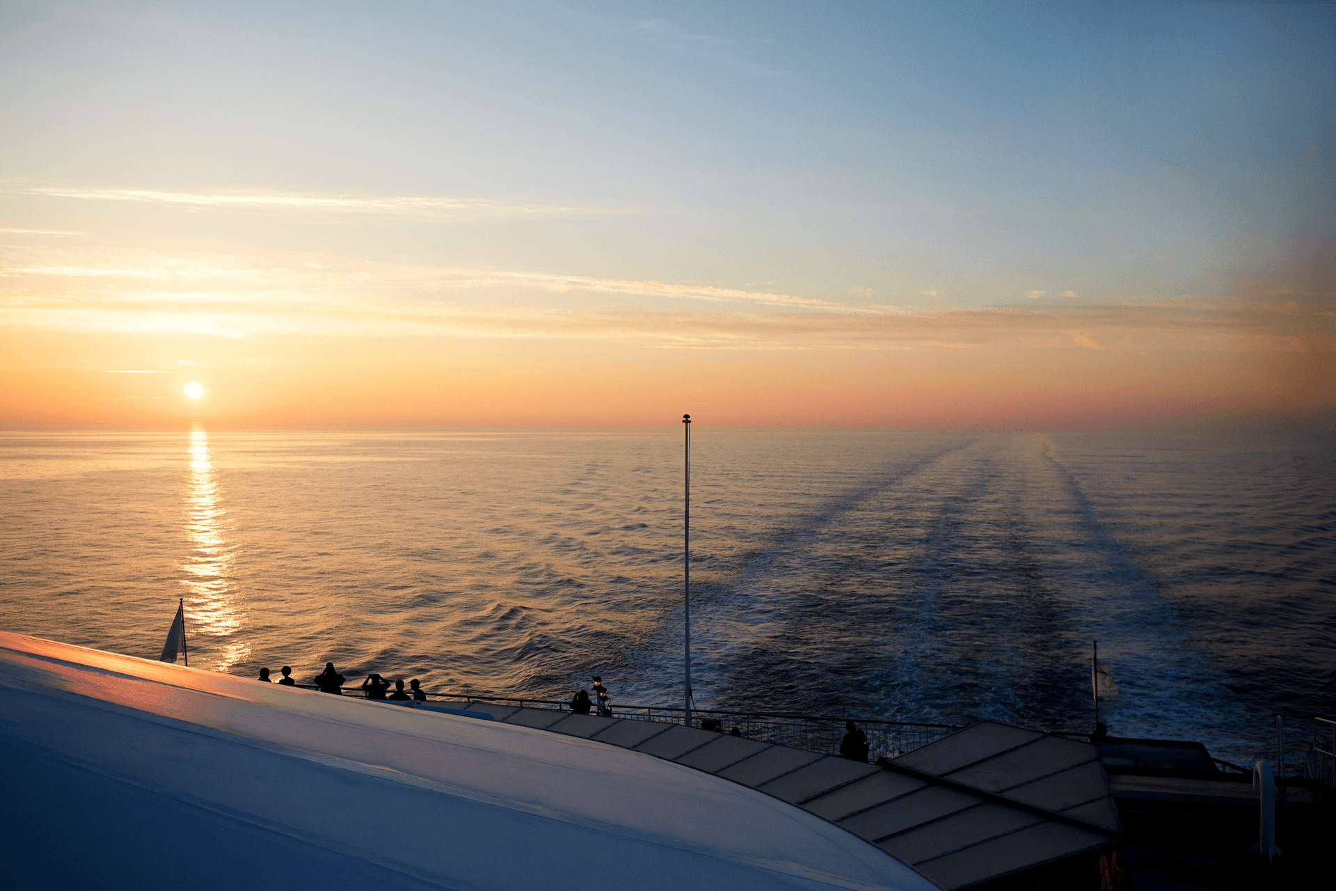 A DFDS vessel sailing on the sea, looking from the backside, with the sunset in the background