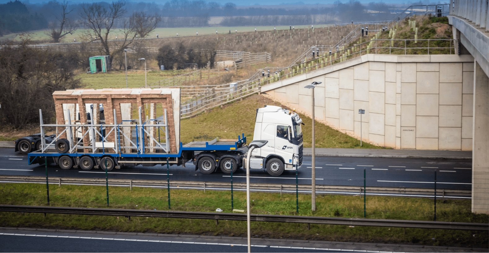A DFDS truck transporting a house façade approaches a bridge passage on the highway