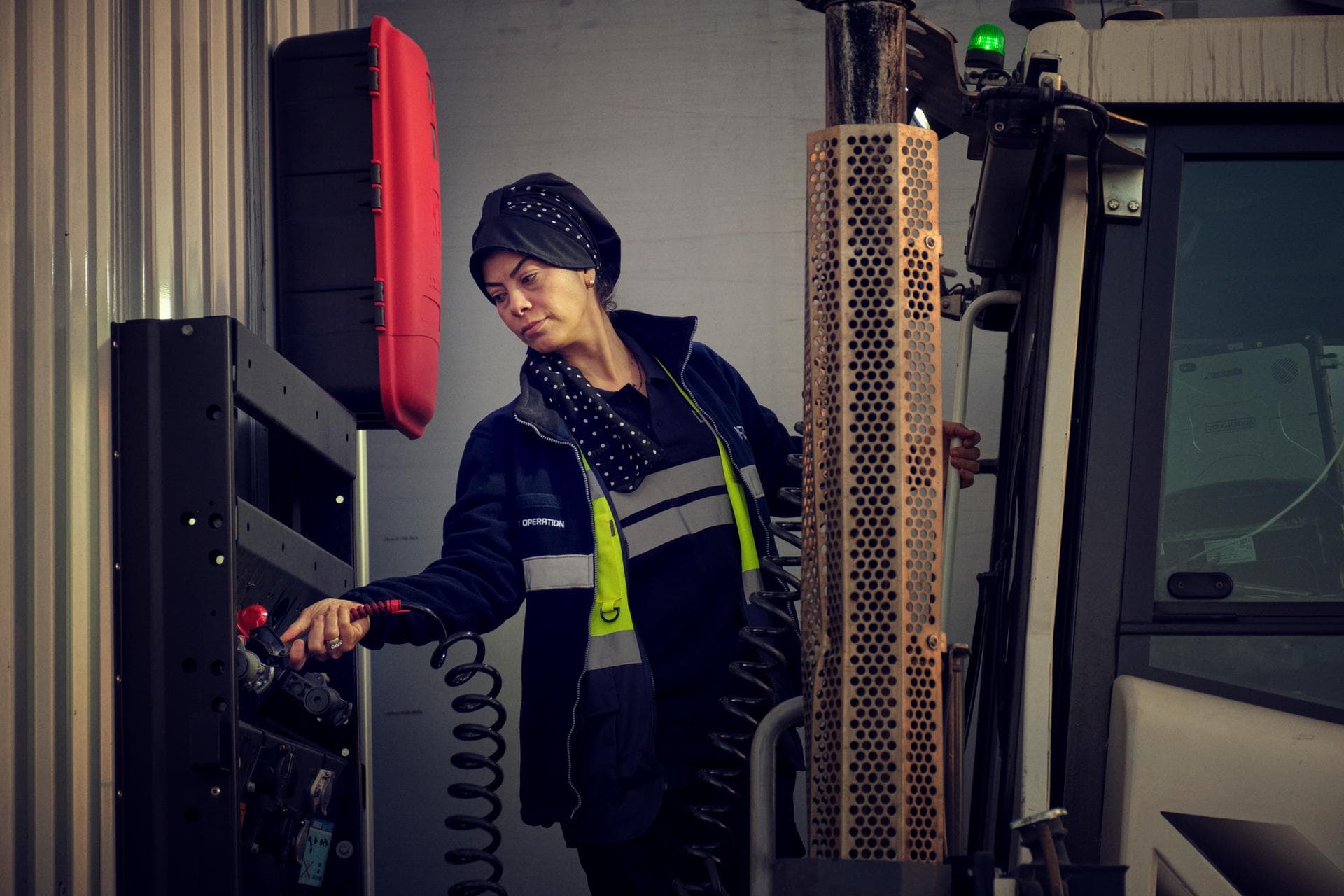 Operational staff warehousing and terminals: female worker in DFDS clothing, disconnecting the cable from a  trailer, standing at the back of a tug master