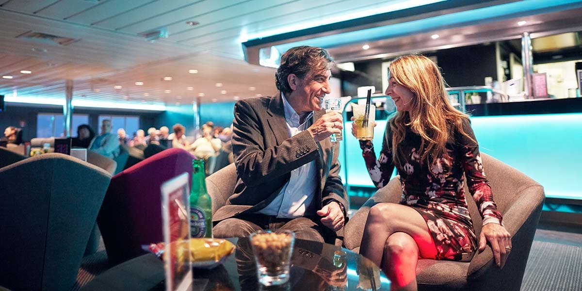 Zadowolona para siedzi w barze i pije drinki, w tle widać bar